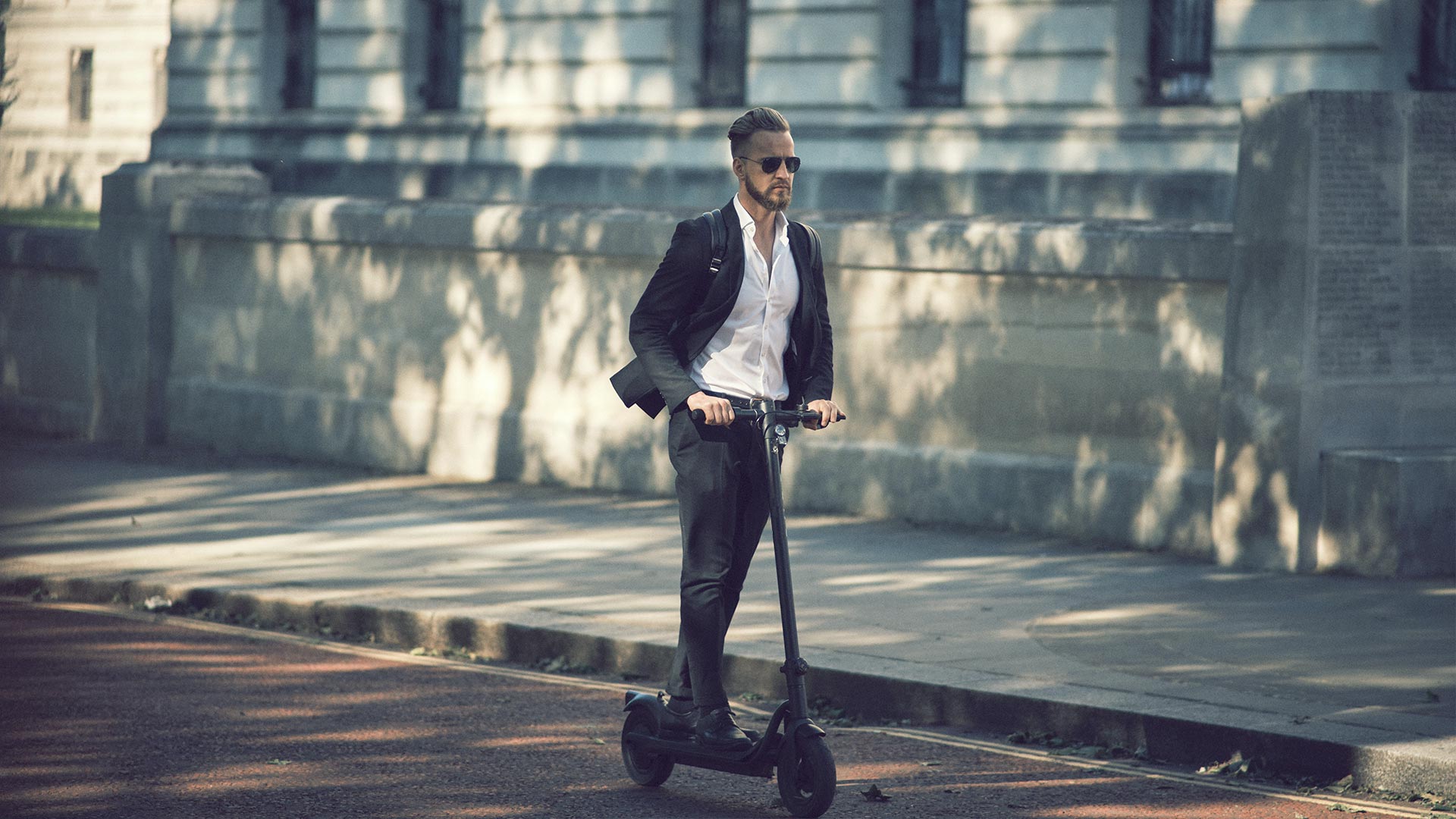 En kledd mann på elektrisk scooter, som glir gjennom bymiljøet.